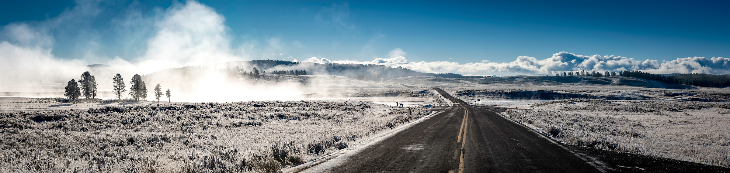 396 megapixels! A very high resolution, large-format VAST photo print of snow in Yellowstone National Park with a road heading off into the distance and trees on a hill; photo created by Justin Katz in Wyoming