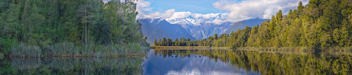 1,599 megapixels! A very high resolution, gigapixel panorama photo of a beautiful lake with trees on the banks in the foreground and a snowy mountain range in the background; landscape photograph created by John Freeman at Lake Matheson on South Island, New Zealand.