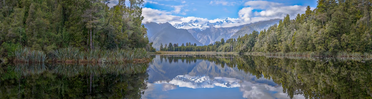 611 megapixels! A very high resolution, large-format panorama photo of a beautiful lake in nature with calm water in the foreground, forests on the banks in the midground and a snowy mountain range in the background; landscape photograph created by John Freeman at Lake Matheson on South Island, New Zealand.